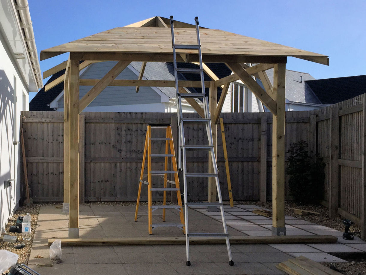 Gazebo erected on supporting posts with roof being assembled